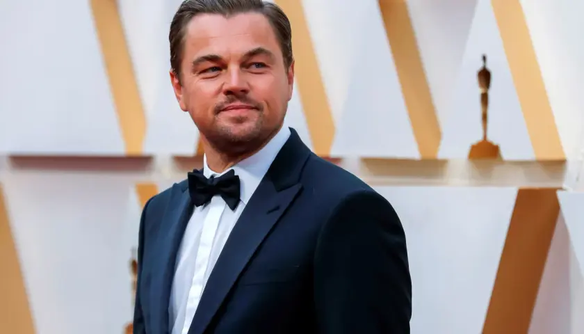 Leonardo DiCaprio, elegante in smoking, sorride con orgoglio, un'immagine che evoca i suoi numerosi premi vinti.