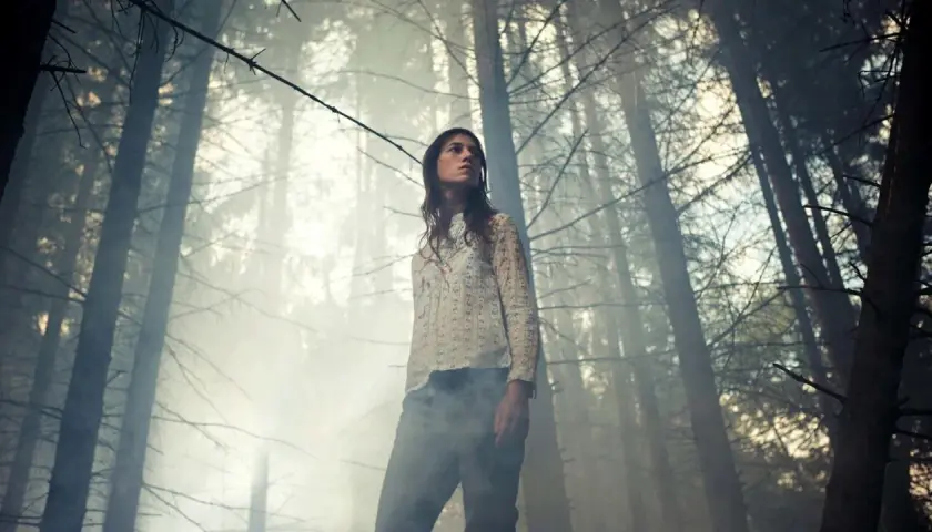 Una giovane donna in una foresta nebbiosa, con un'espressione pensierosa. Potrebbe essere una scena che evoca un' antichrist spiegazione, un'oscura profezia che si manifesta.