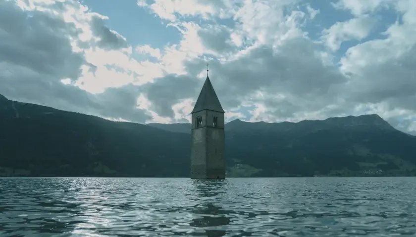 Torre sommersa nel lago, un'icona di Curon. Le recensioni la descrivono come un luogo suggestivo e malinconico, con montagne sullo sfondo.