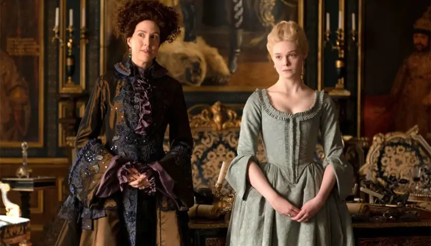 Due donne in abiti storici, una con capelli ricci e un vestito scuro elaborato, l'altra con capelli biondi raccolti e un abito verde chiaro. Le loro espressioni suggeriscono un momento di tensione, forse in attesa di grandi recensioni.