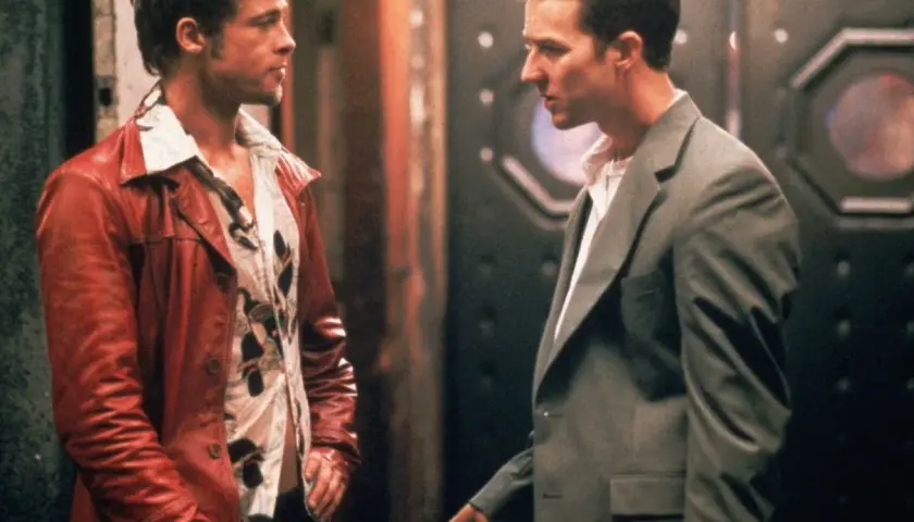 Il narratore di Fight Club, con la sua giacca rossa, parla con un uomo in completo grigio.