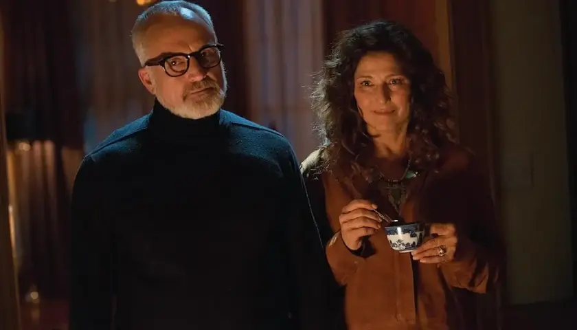 Coppia anziana in un interno buio, lui con occhiali e dolcevita nero, lei sorride con una tazza in mano. Sembra il **get out finale**.