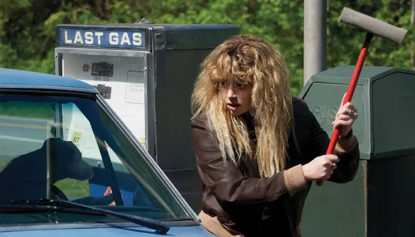 La protagonista di Poker Face, Nadia Vulvokov, con i suoi capelli biondi spettinati, impugna un tergivetro rosso davanti a una pompa di benzina "Last Gas".