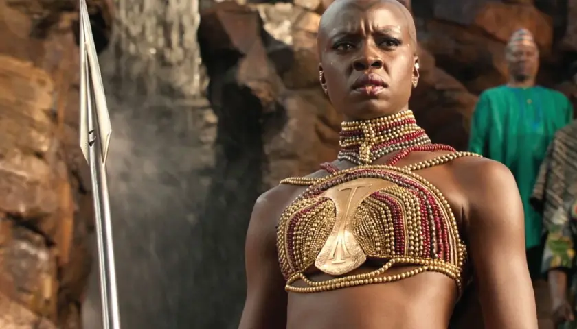 Guerriera Wakandiana con lancia, indossa un elaborato costume dorato e rosso, degno di un premio Oscar ai migliori costumi.