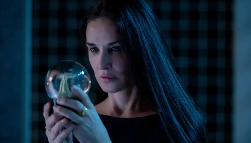 Donna con lunghi capelli scuri osserva una sfera luminosa, un'immagine che evoca mistero e riflessione, come in una recensione di "The Substance".
