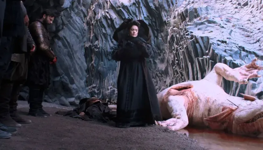 Una donna in nero osserva un mostro acquatico morto, con guerrieri al fianco. Scena da "Il racconto dei racconti recensione".