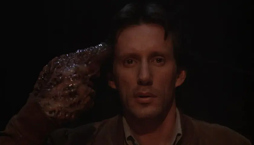 Un uomo con una mano mutata, simile a un tumore, punta alla tempia. Un'immagine disturbante che riflette il videodrome significato.