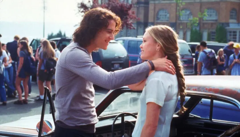 Il cast di "10 cose che odio di te" con Heath Ledger e Julia Stiles che si guardano sorridendo vicino a un'auto.