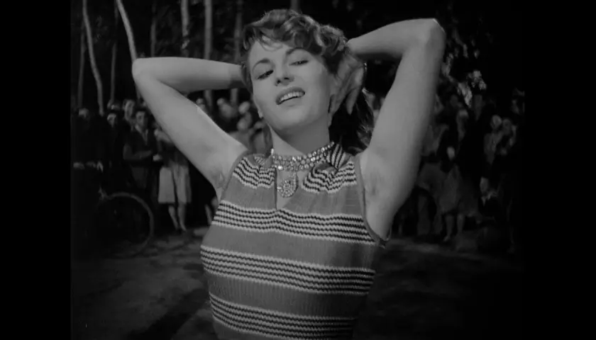 Una donna con le braccia alzate, un sorriso sulle labbra e un'espressione che evoca il "riso amaro significato". Sullo sfondo, una folla indistinta.