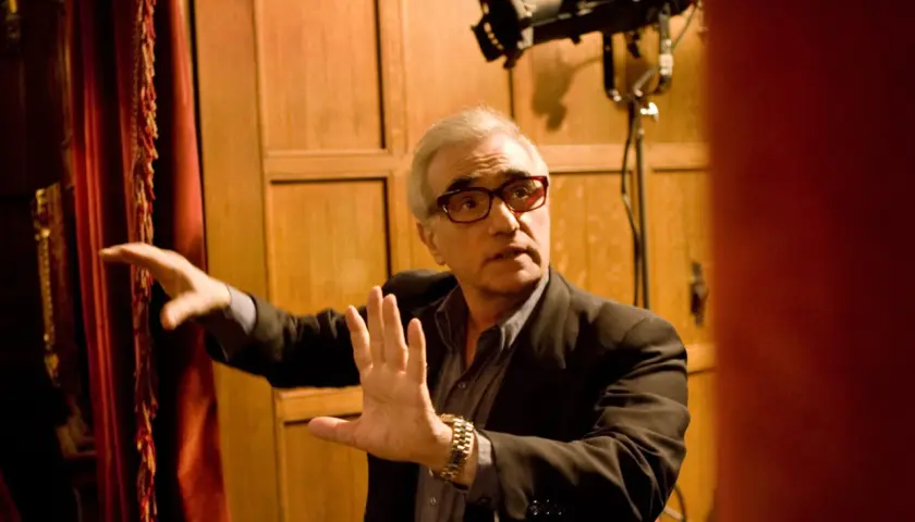 Martin Scorsese, con occhiali rossi, dirige sul set di Shutter Island. Le sue mani sono alzate, come a dare indicazioni.