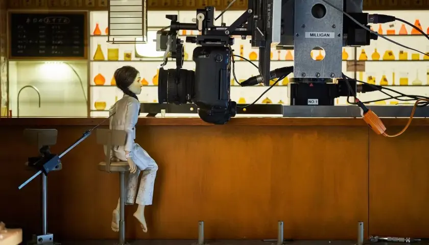 Bambola seduta su uno sgabello, pronta per essere animata in stop motion. La telecamera è posizionata sopra di lei, pronta a catturare ogni movimento.