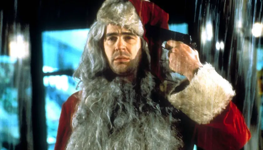 Un uomo con barba e cappello da Babbo Natale tiene una pistola puntata alla tempia. Sembra una scena da "Una poltrona per due Babbo Natale".
