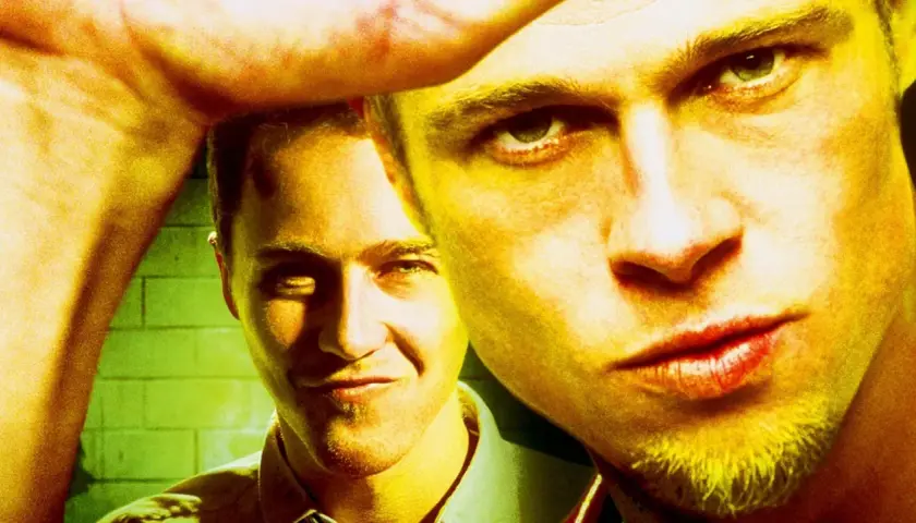 Primo piano di due uomini, uno con uno sguardo intenso, l'altro sorride. L'immagine evoca il **fight club significato** di ribellione e ricerca di identità.