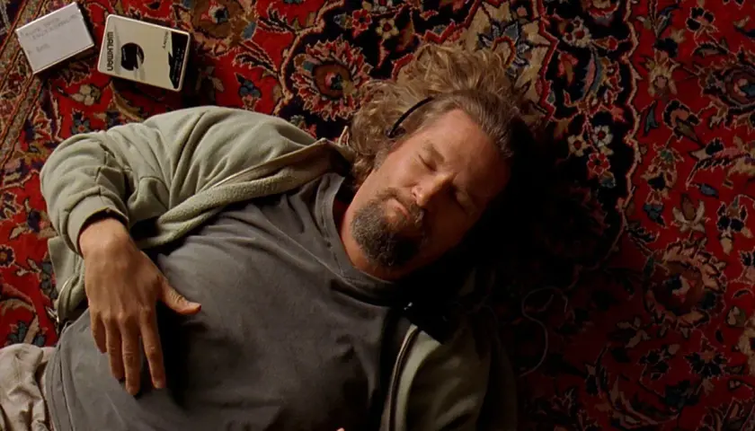 Un uomo con cuffie dorme su un tappeto persiano, accanto a un Walkman. Un'immagine iconica che evoca le recensioni de "Il Grande Lebowski".