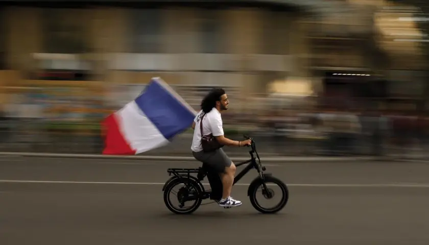 Uomo in bici sfreccia con bandiera francese, un'immagine che sfugge alle recensioni sull'odio.