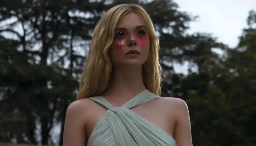 Ragazza con trucco glitterato e vestito verde pallido, un'immagine che evoca il significato di "The Neon Demon" e la sua ossessione per la bellezza.