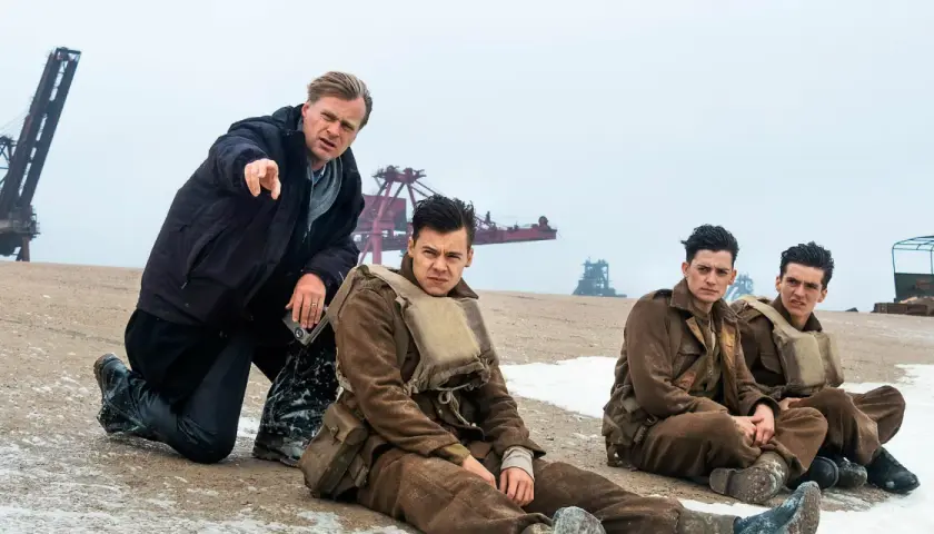 Il cast di Dunkirk, con Christopher Nolan che dirige i giovani soldati seduti sulla spiaggia.
