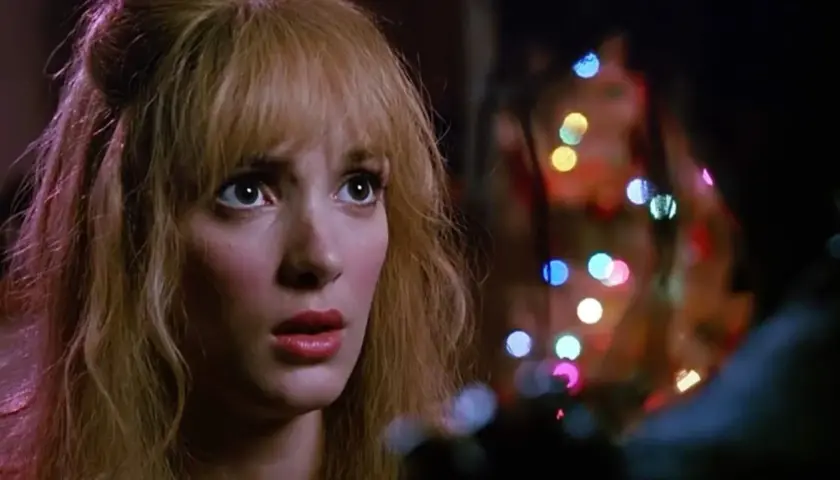Kim, con sguardo preoccupato, è illuminata da luci colorate, un momento intenso con Edward mani di forbice.