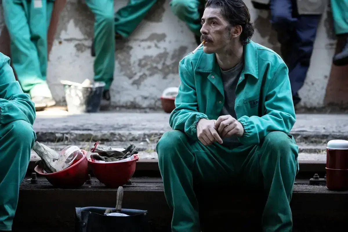 Uomo con baffi, in tuta verde, fuma una sigaretta. Le sue mani sono giunte, sembra pensieroso. Le recensioni per la palazzina LAF potrebbero essere simili.