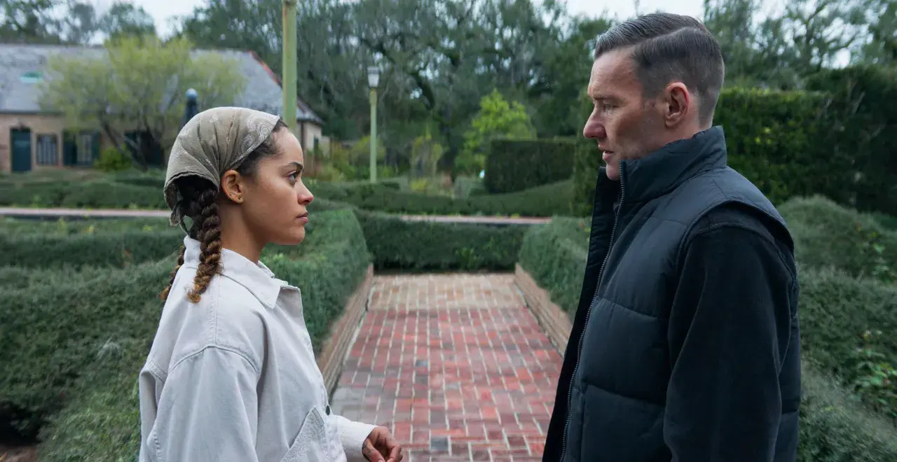 Due persone si guardano in un giardino curato, con siepi e un vialetto di mattoni. Le recensioni per "il maestro giardiniere" potrebbero descrivere scene come questa.
