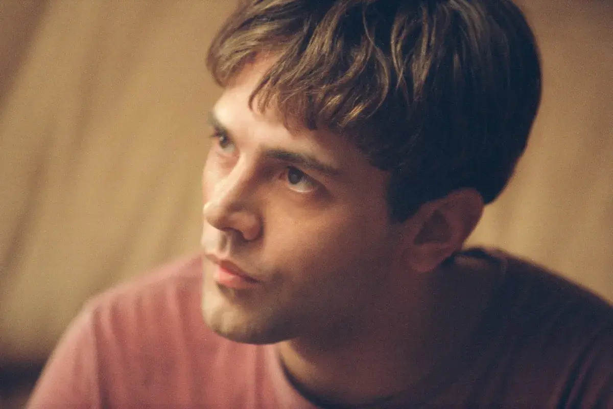 Primo piano di un giovane uomo con capelli castani e una maglietta rosa. Potrebbe essere Xavier Dolan fidanzato.