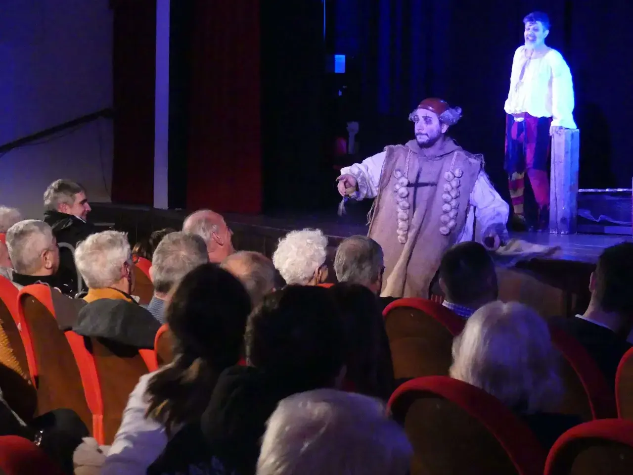 Attori in costume sul palco, il pubblico osserva la rappresentazione teatrale, infrangendo la **quarta parete teatro**.