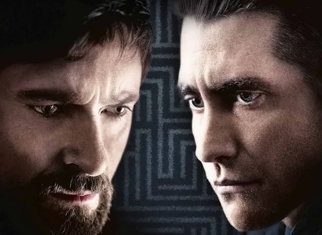 Primo piano dei volti intensi del cast di Prisoners, Hugh Jackman e Jake Gyllenhaal, con uno sfondo a labirinto.