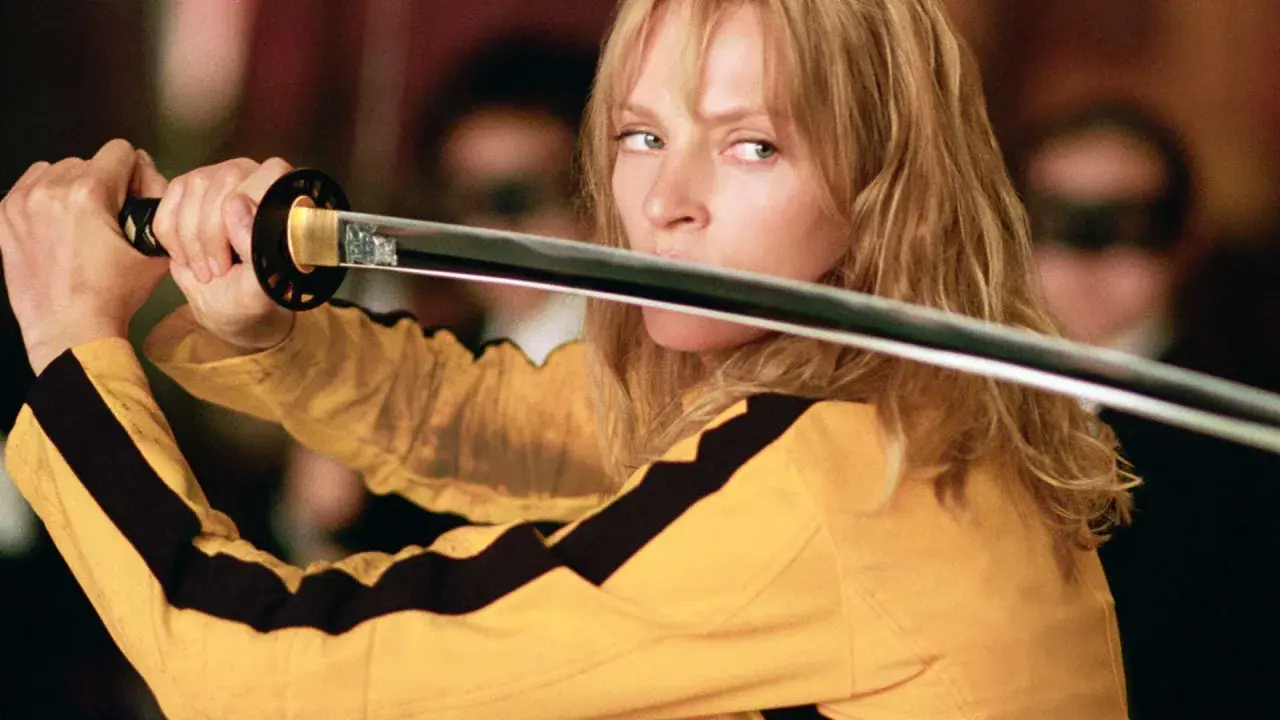 La Sposa, con la sua iconica tuta gialla, impugna la katana. Il suo sguardo è intenso, pronto a vendicarsi. Kill Bill: la benda sull'occhio è un monito.