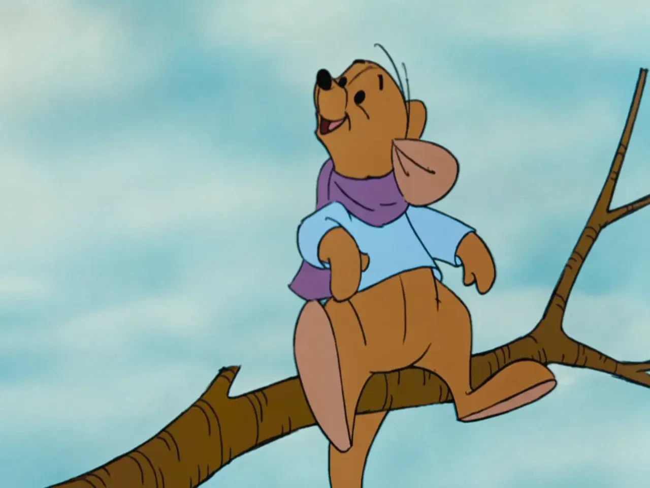 Winnie the Pooh, interpretato da Jim Cummings, siede su un ramo con una sciarpa viola e una camicia azzurra.