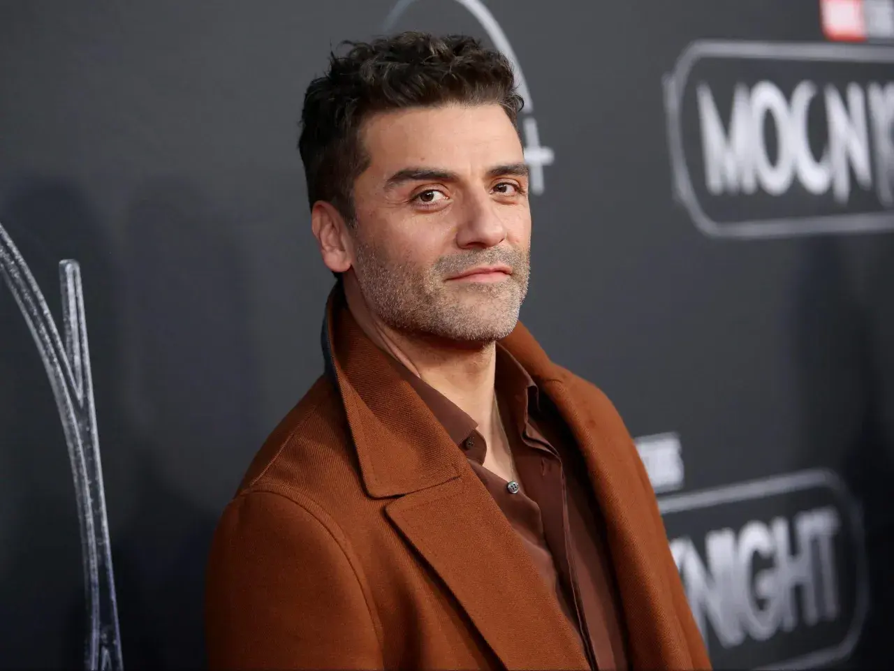 Oscar Isaac, l'attore di Moon Knight, posa con un cappotto marrone.