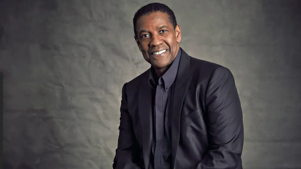 Ritratto di Denzel Washington, attore e doppiatore, con un sorriso caloroso e un abito scuro.