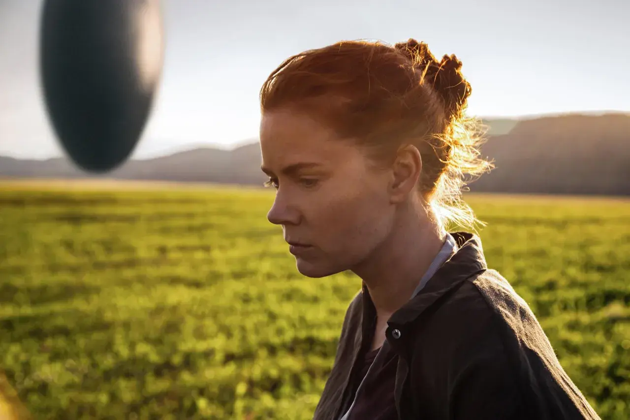 Donna con capelli rossi guarda un misterioso oggetto ovale fluttuante, simbolo dell'arrival linguaggio.