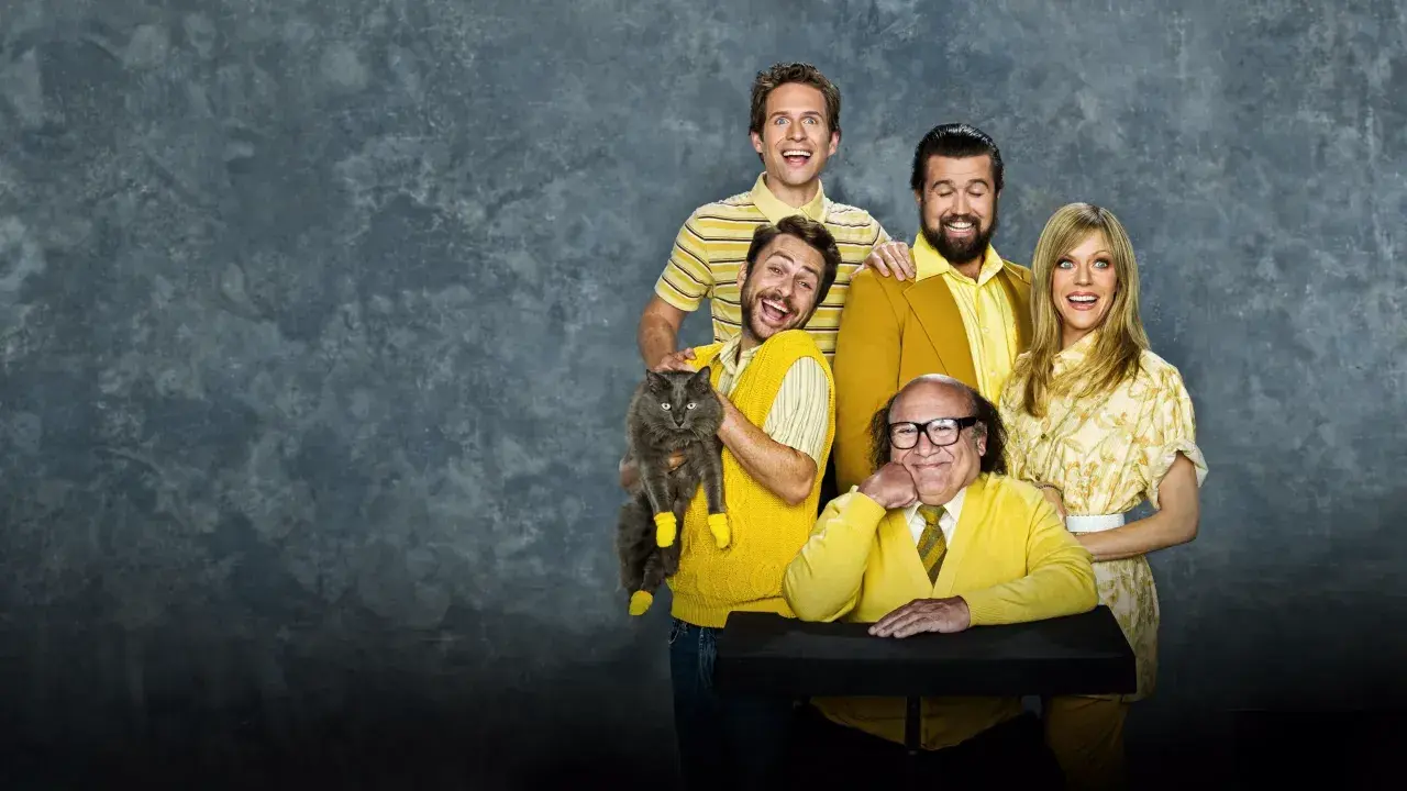 Il cast di "C'è sempre il sole a Philadelphia" posa sorridendo, con Charlie che tiene un gatto grigio con calzini gialli.