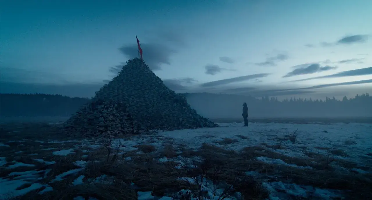 Un uomo solitario osserva un'enorme piramide di teschi in un paesaggio innevato. Un'immagine che evoca le recensioni de "The Revenant".