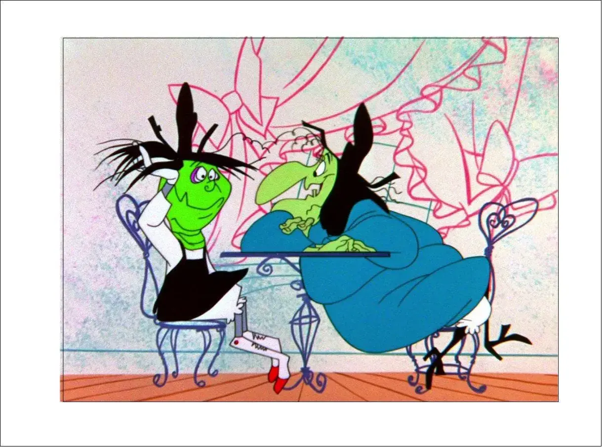 Due streghe, una verde e una con la pelle verde, sedute a un tavolo. La strega Hazel, con i capelli neri e un vestito blu, sembra annoiata.