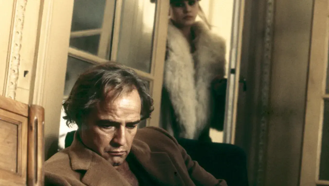 Marlon Brando pensieroso, sullo sfondo Maria Schneider in pelliccia. Scena iconica di "Ultimo tango a Parigi", la scena del burro.