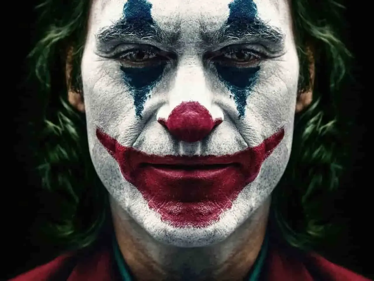 Il volto truccato da clown, con un sorriso rosso e lacrime blu, incarna il vero joker significato: la follia che nasce dal dolore.
