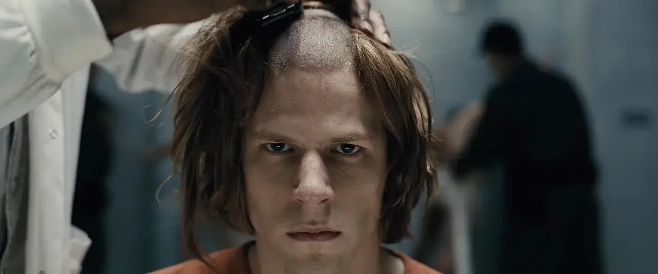 Un primo piano intenso di Jesse Eisenberg in un film, mentre gli rasano i capelli.