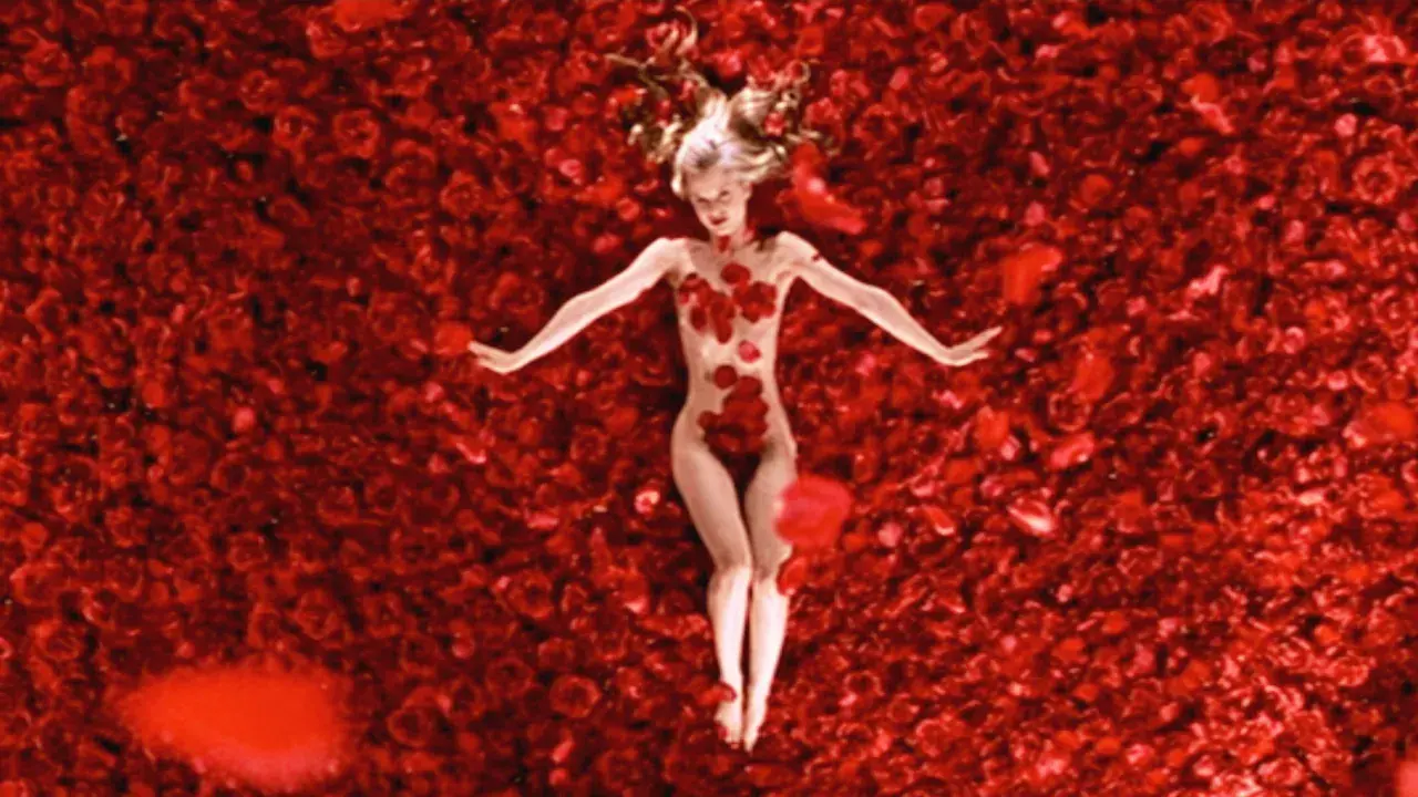 Una donna giace su un letto di rose rosse, un'immagine iconica che evoca la bellezza e la complessità di "American Beauty recensione".
