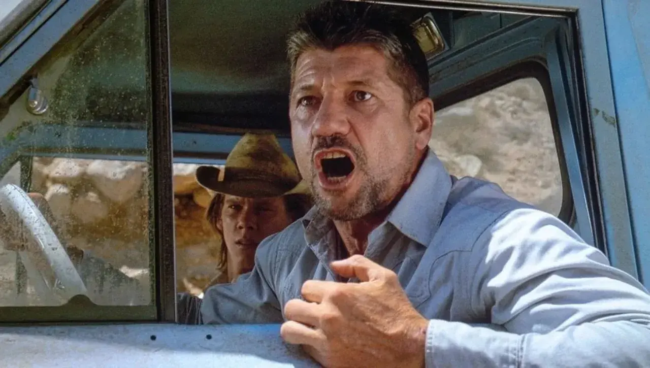 Fred Ward, attore noto per film d'azione, con espressione angosciata in auto. La sua causa morte è stata una malattia.