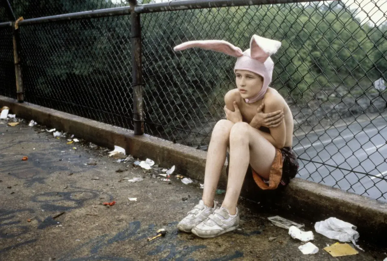 Bambino con cappello da coniglio seduto su un marciapiede sporco, un'immagine che evoca la trama di Gummo.