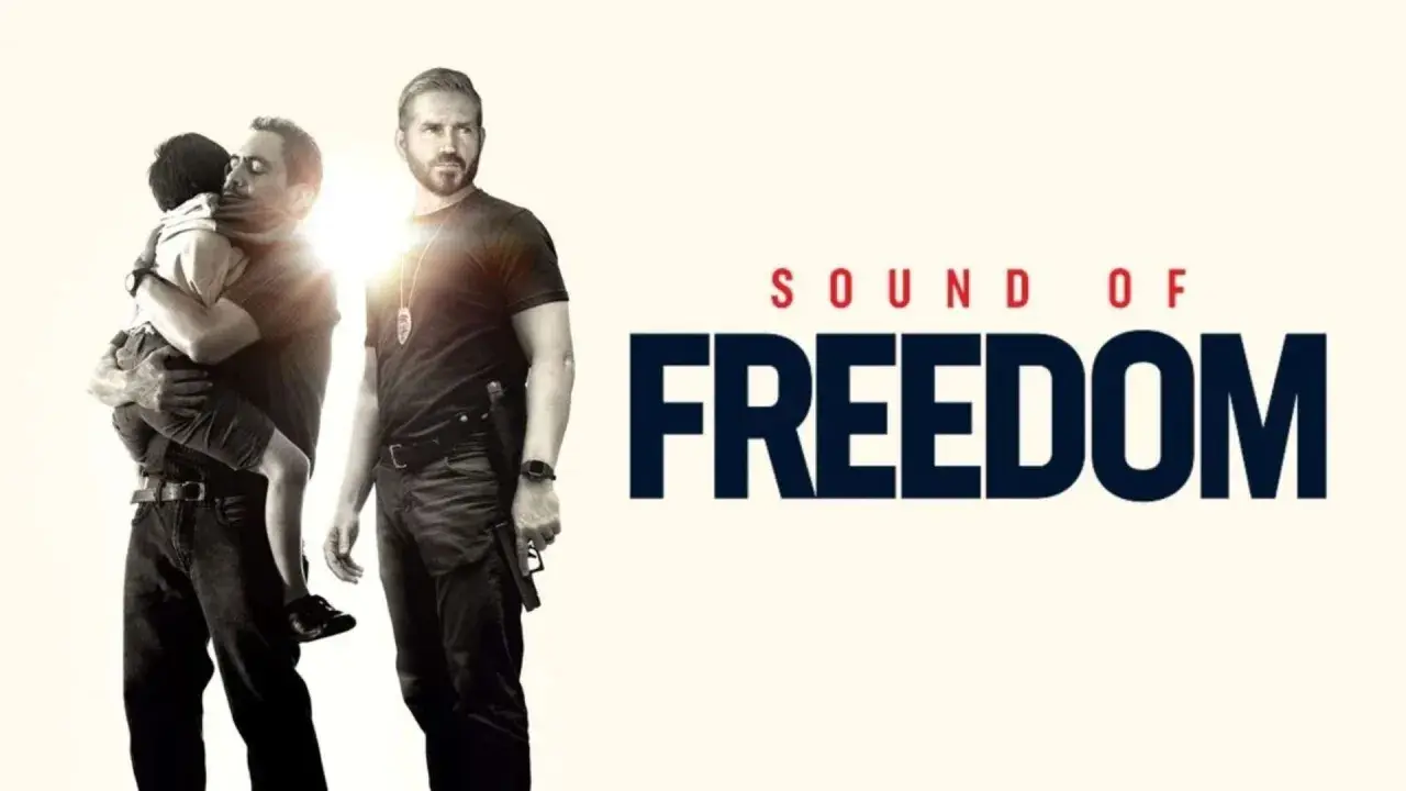 Un uomo abbraccia un bambino, mentre un altro uomo con una pistola guarda. Titolo: Sound of Freedom. Le recensioni lodano questo film.