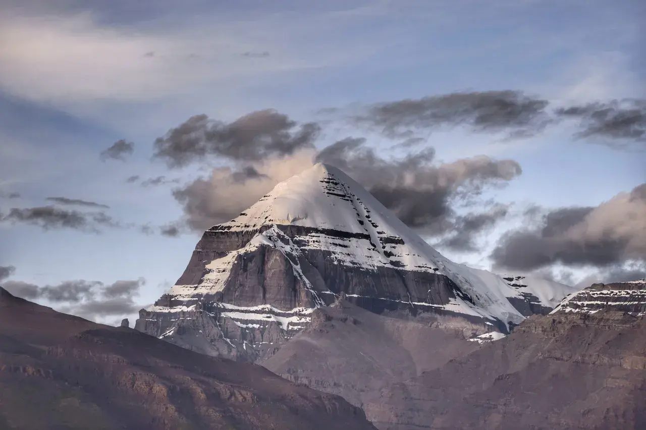 La montagna sacra spiegazione: il maestoso Kailash, coperto di neve, si erge tra nuvole scure e un cielo crepuscolare, simbolo di spiritualità e mistero.