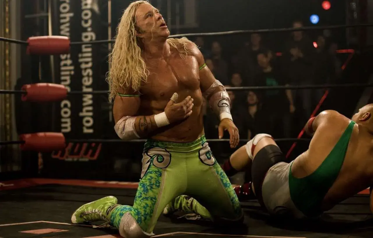 Randy the Ram, il wrestler dai lunghi capelli biondi, in ginocchio sul ring, guarda verso l'alto con espressione intensa.