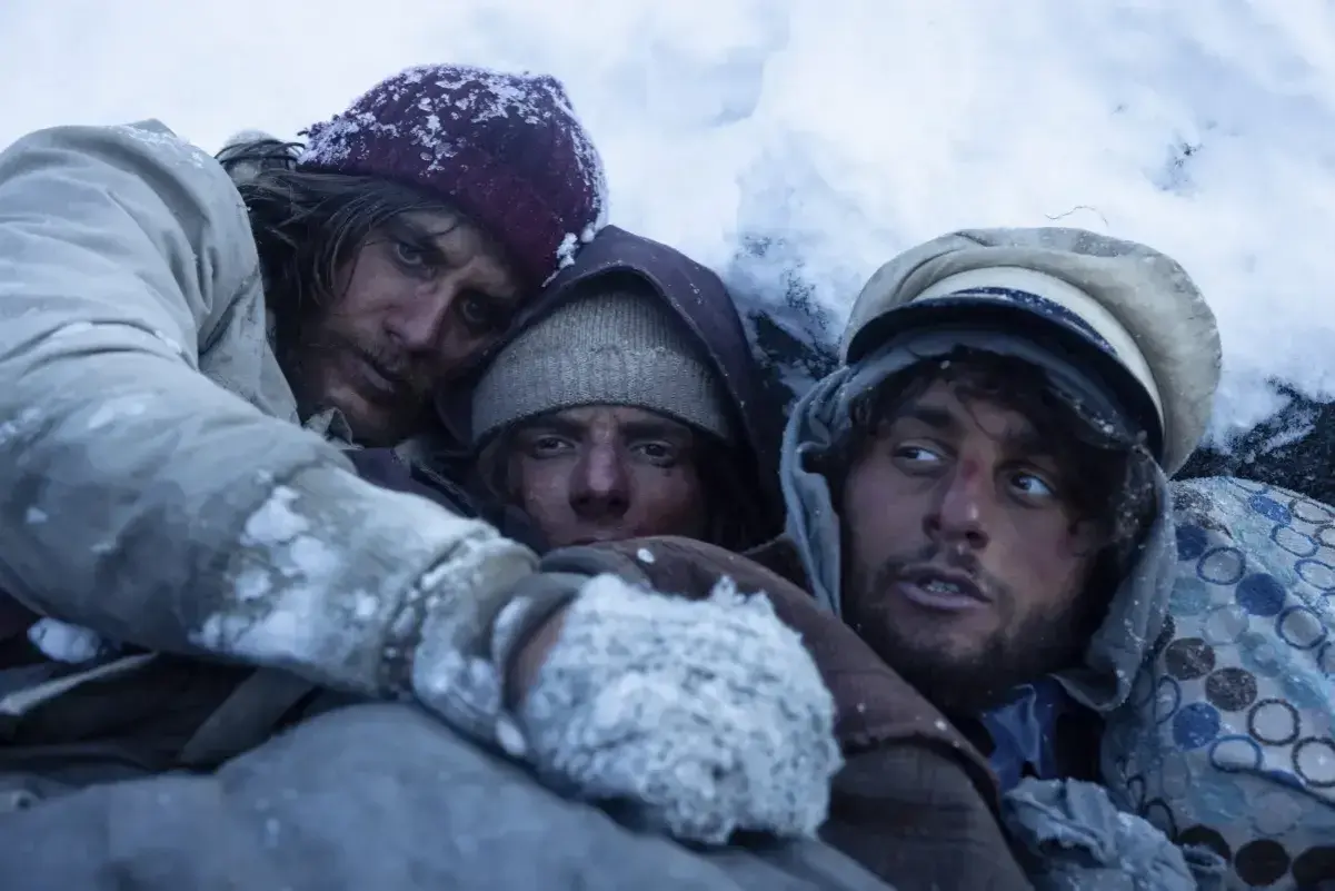 Tre uomini stremati nel gelo, un'immagine che evoca le recensioni de "La società della neve", la lotta per la sopravvivenza.