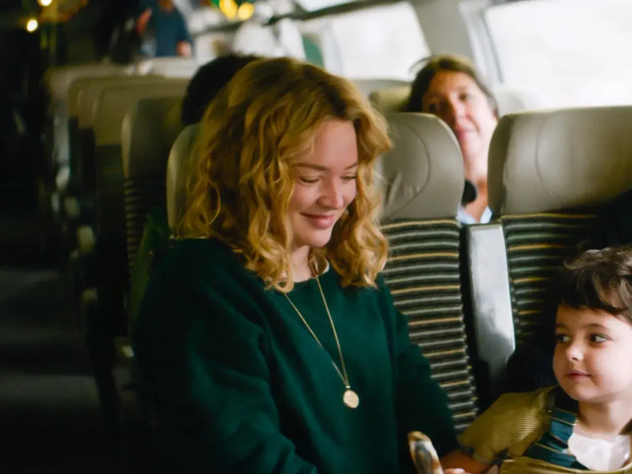 Una donna sorride mentre guarda un bambino su un treno. Le recensioni de "I figli degli altri" lodano questa scena.