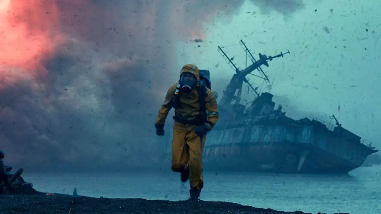 Uomo in tuta gialla corre su una spiaggia desolata, con una nave naufragata sullo sfondo. Le recensioni di Greenland descrivono scene apocalittiche simili.