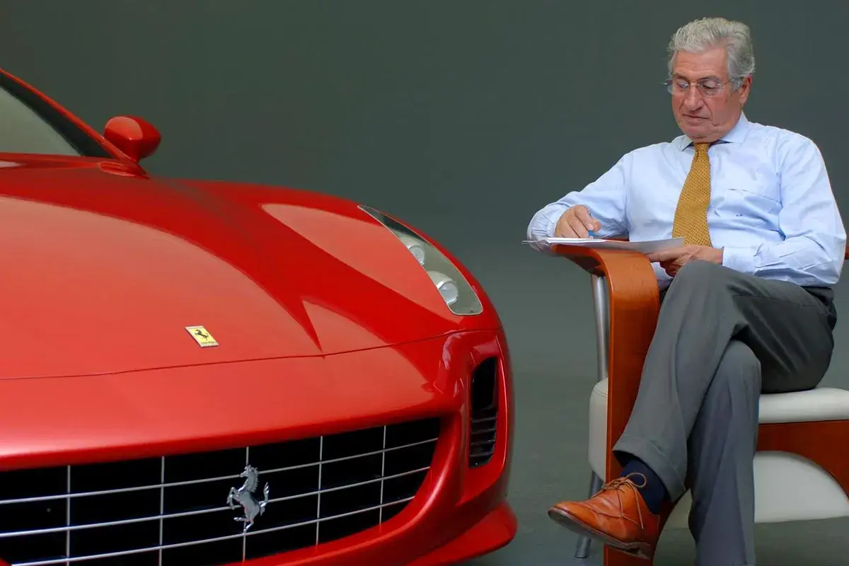 Un uomo d'affari con una cravatta gialla scrive appunti accanto a una Ferrari rossa, forse per le recensioni del film.
