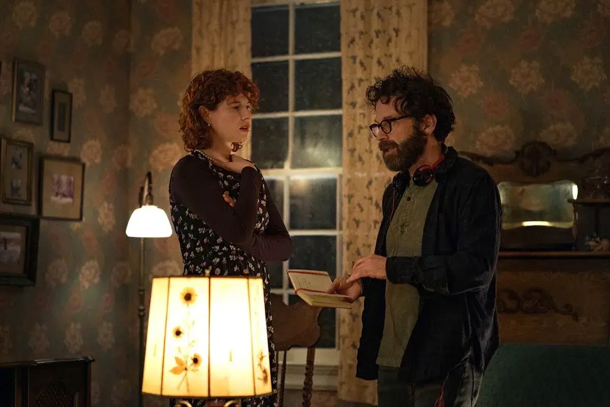 Una donna con capelli rossi e un uomo con occhiali discutono animatamente in una stanza. Lui tiene un quaderno, forse sto pensando di finirla qui recensioni.