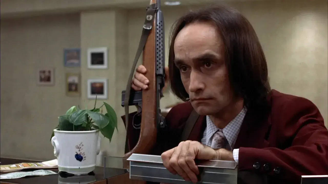 Un uomo con un fucile a tracolla, forse in una scena che ricorda il john cazale funeral, guarda intensamente.